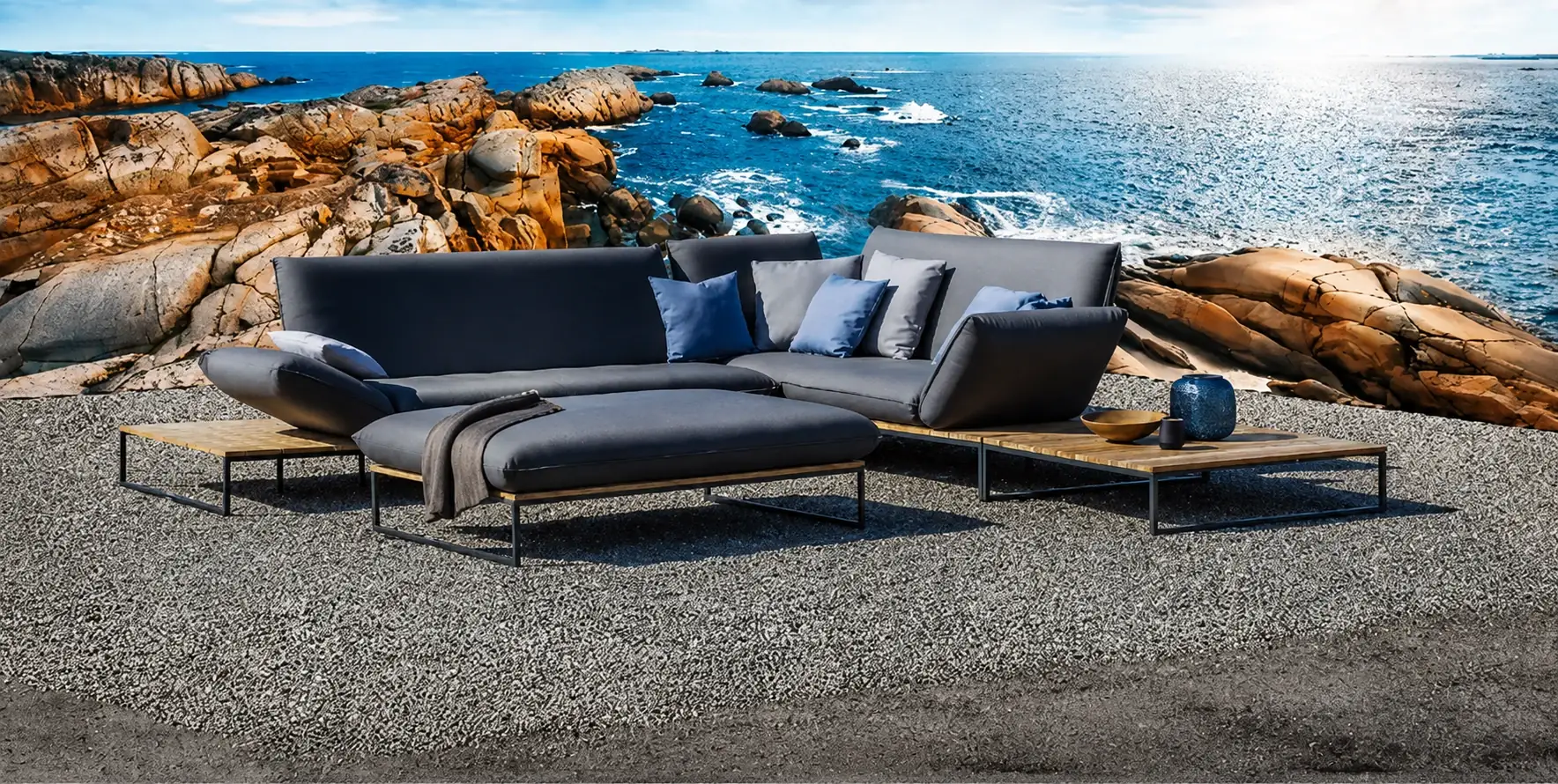 Dark grey modular outdoor sofas on a gravel terrace above a rocky coastline