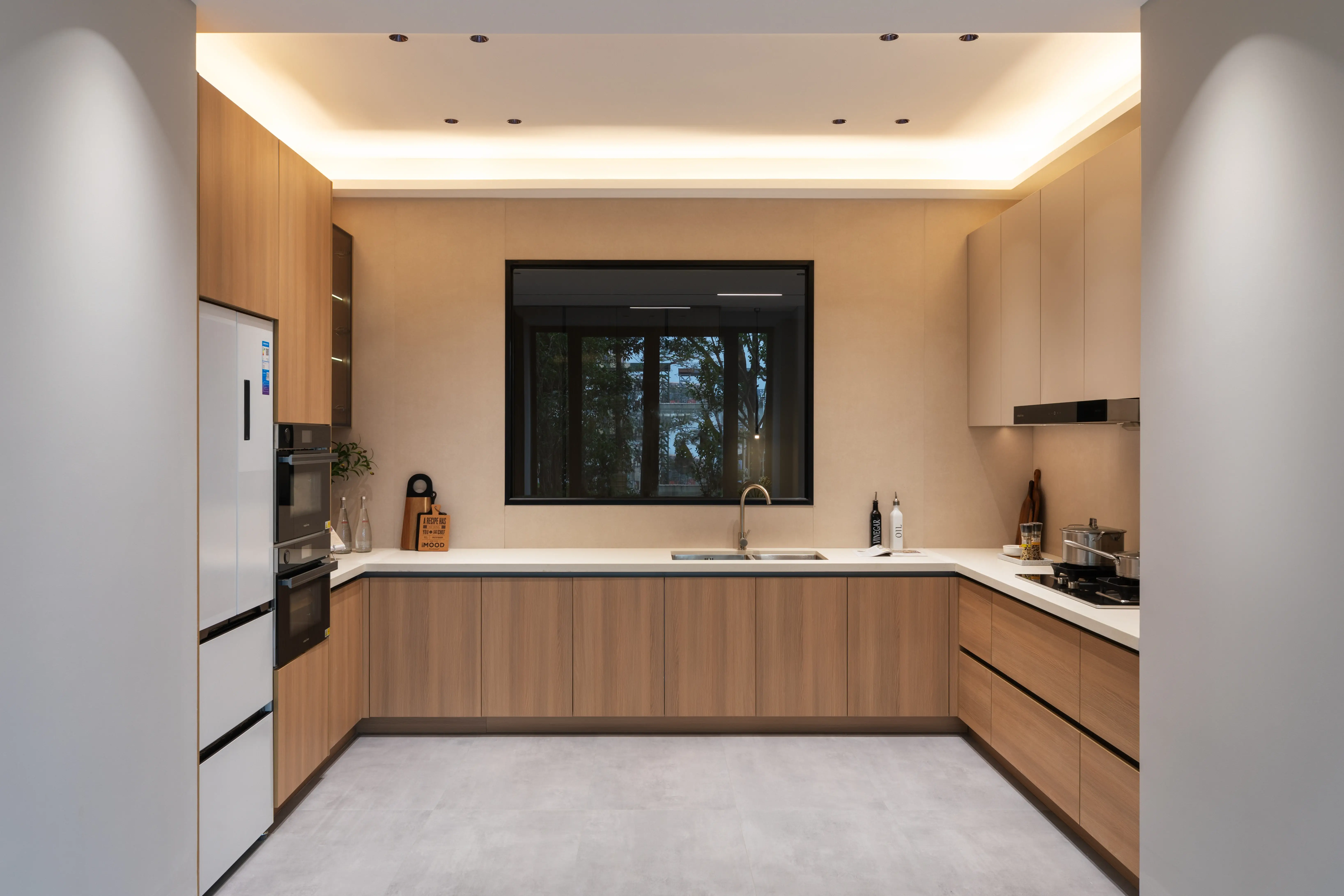 Light oak kitchen with white worktops beneath a garden window