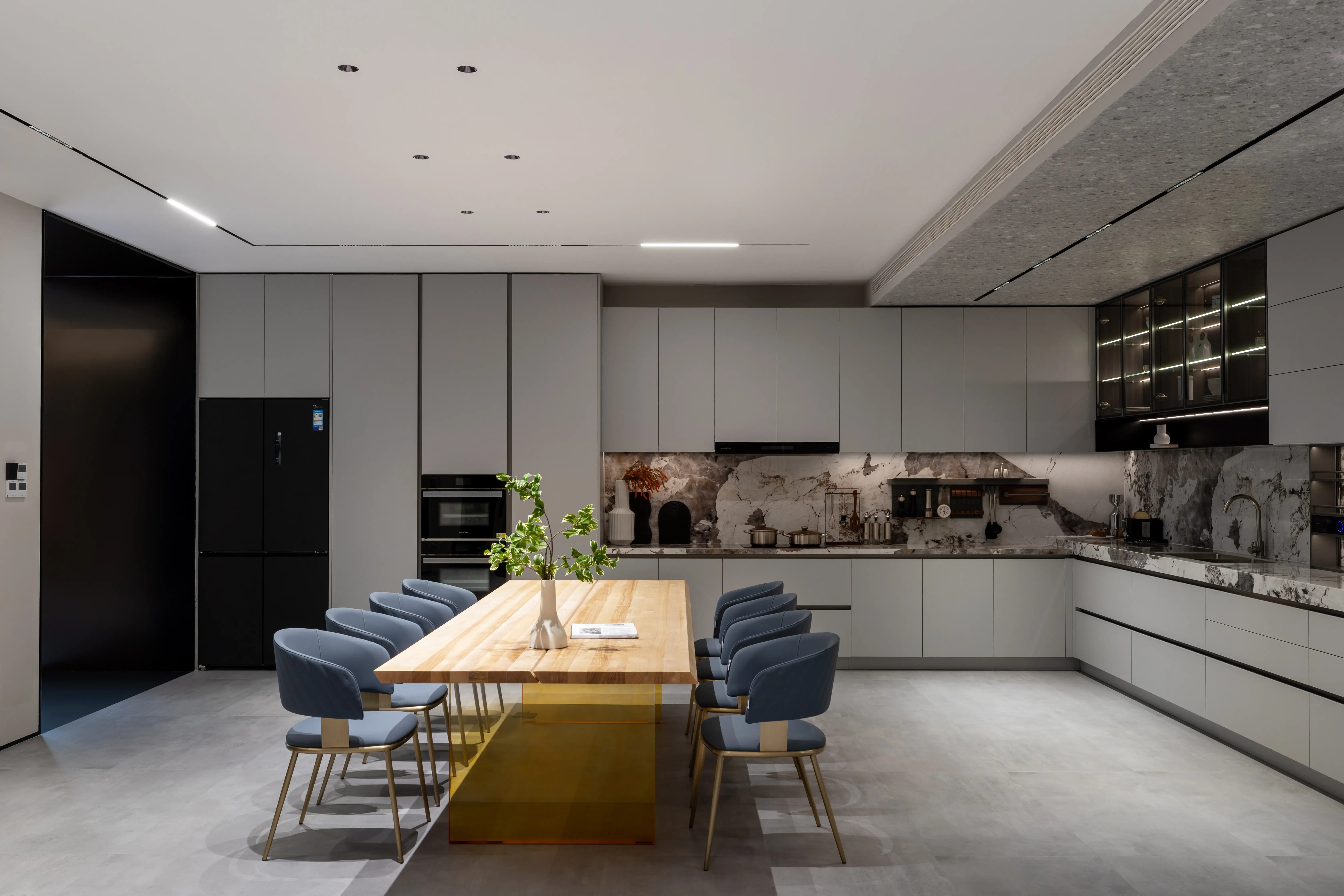 Open-plan grey kitchen with a long dining table and upholstered blue chairs